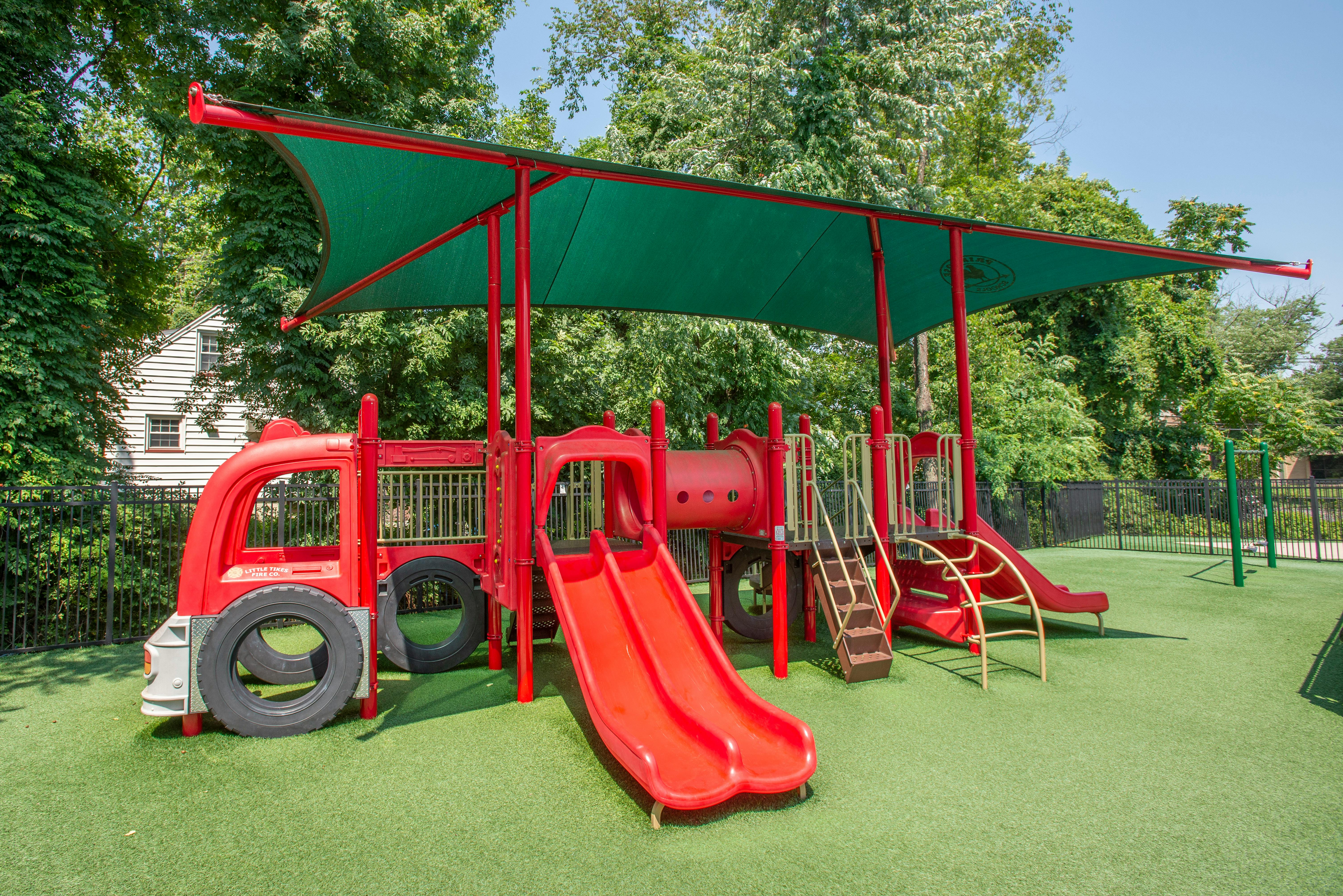 Red playground with slides and a fire truck feature under a green canopy