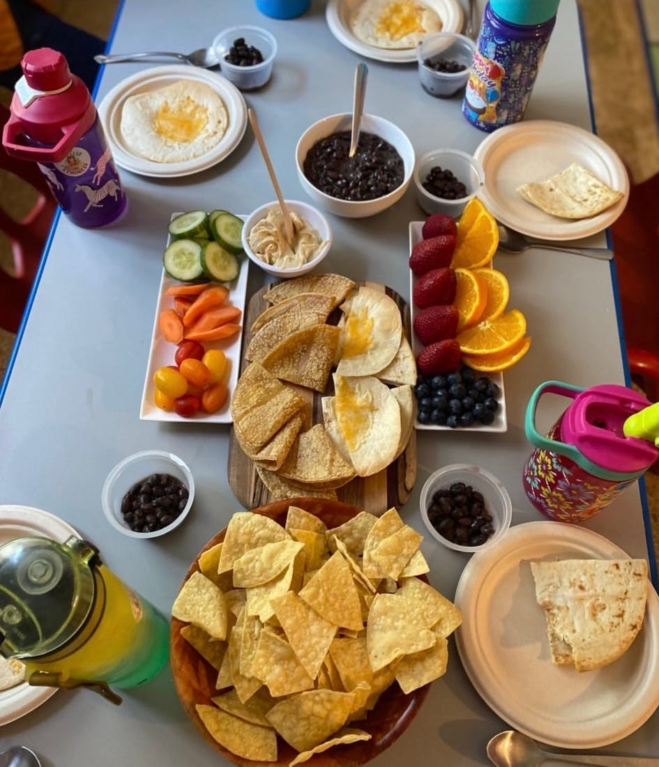 Table with various snacks including chips, fruit, vegetables, and dips