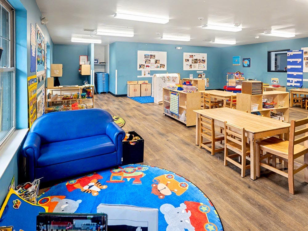 Classroom with small wooden tables and chairs, a blue couch, and a colorful rug