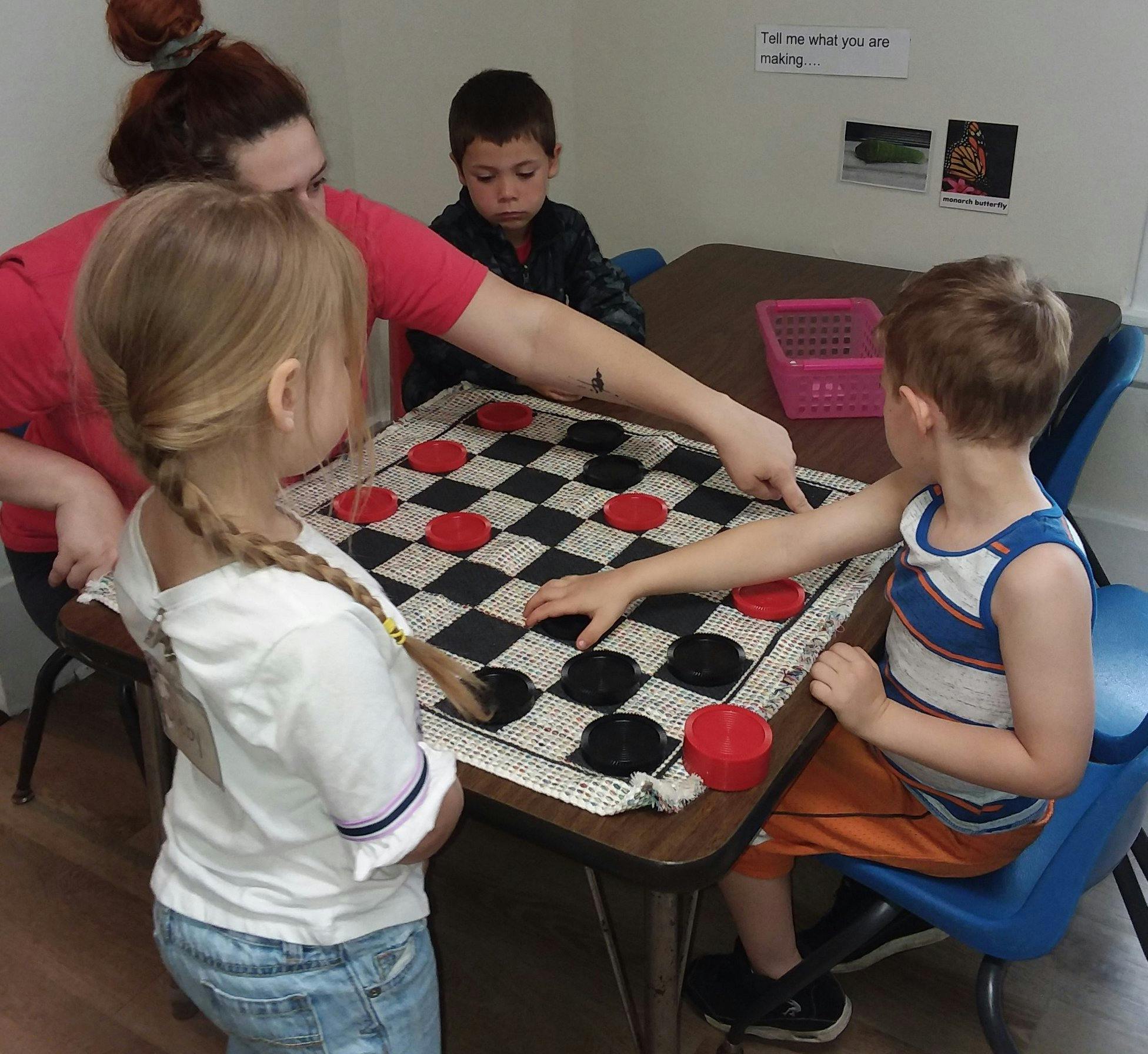 Adult and three children playing checkers at a table