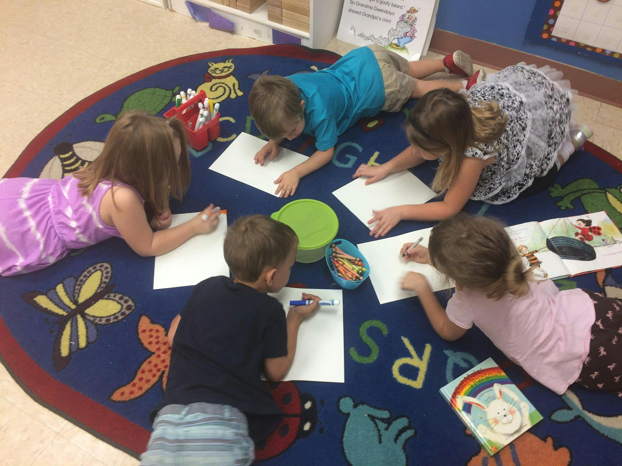Children drawing on paper while lying on a rug