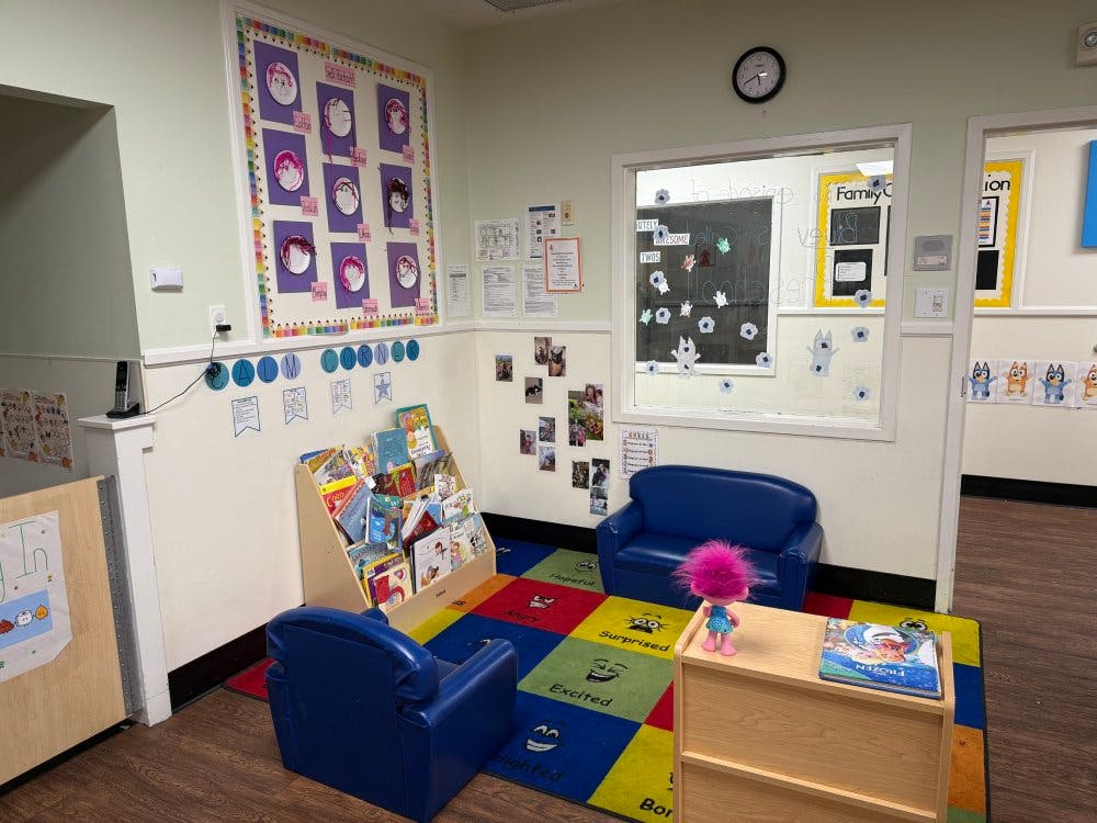 Child's reading nook in a classroom with a bookshelf, small chairs, and a colorful rug