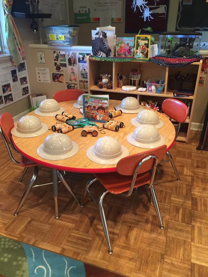 Round table with safari hats, toy binoculars, and a book in a classroom
