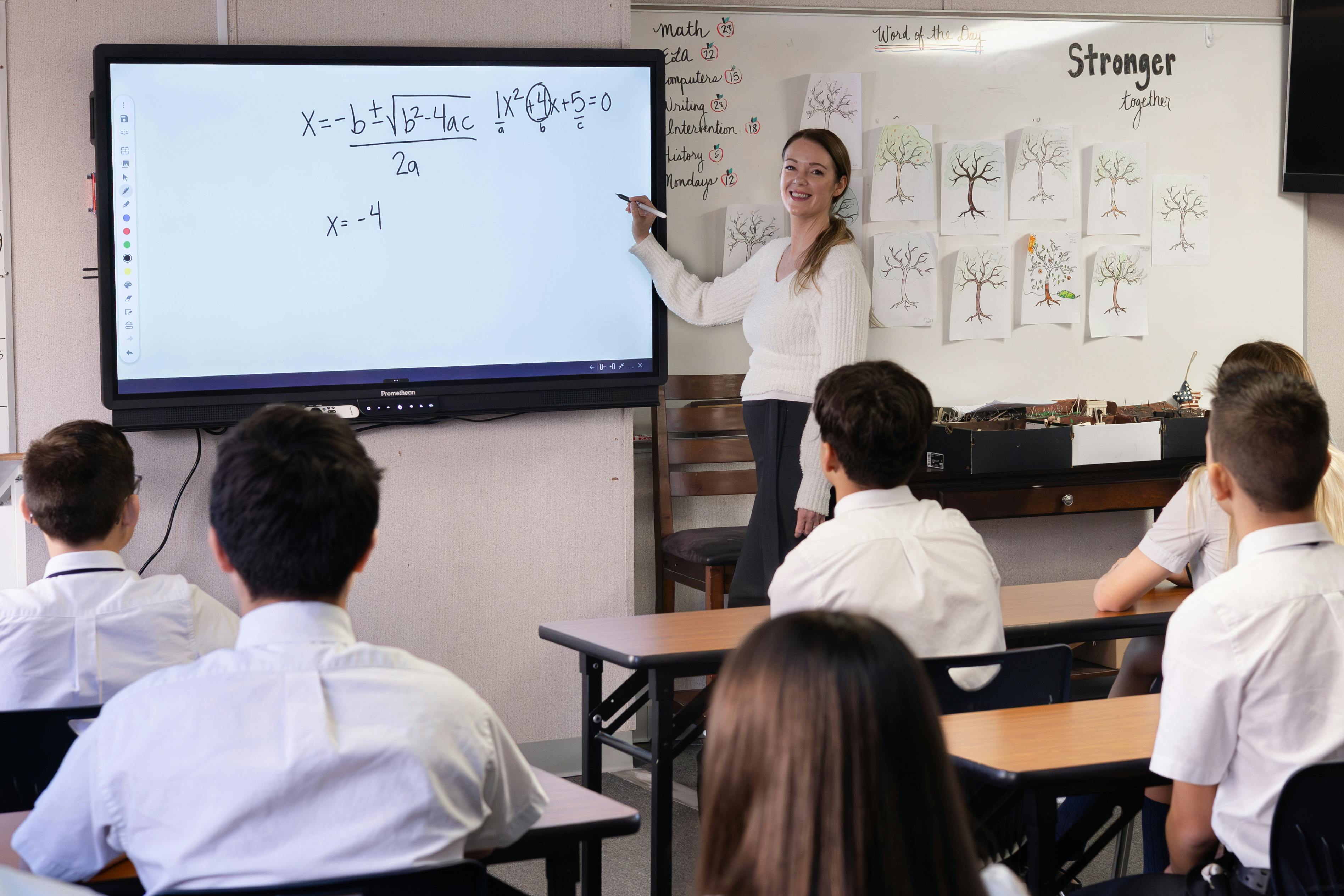 Teacher pointing at a screen with math equations in a classroom with students