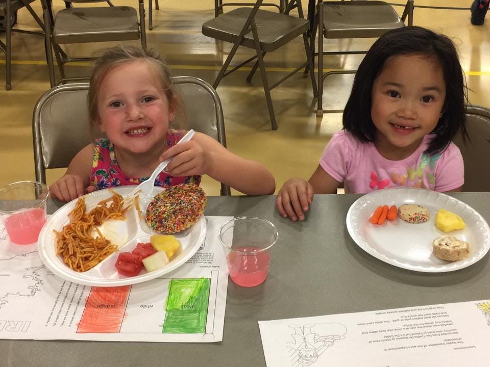 Two children sitting at a table with plates of food and drinks