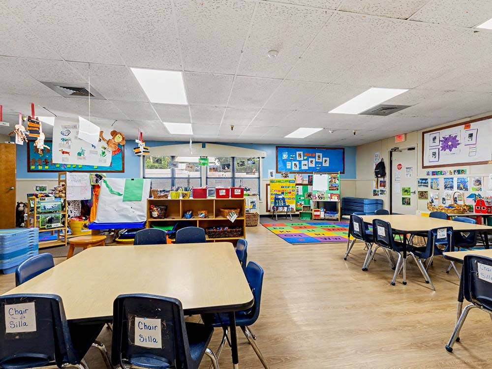 Classroom with small tables and chairs, colorful rug, and bulletin boards