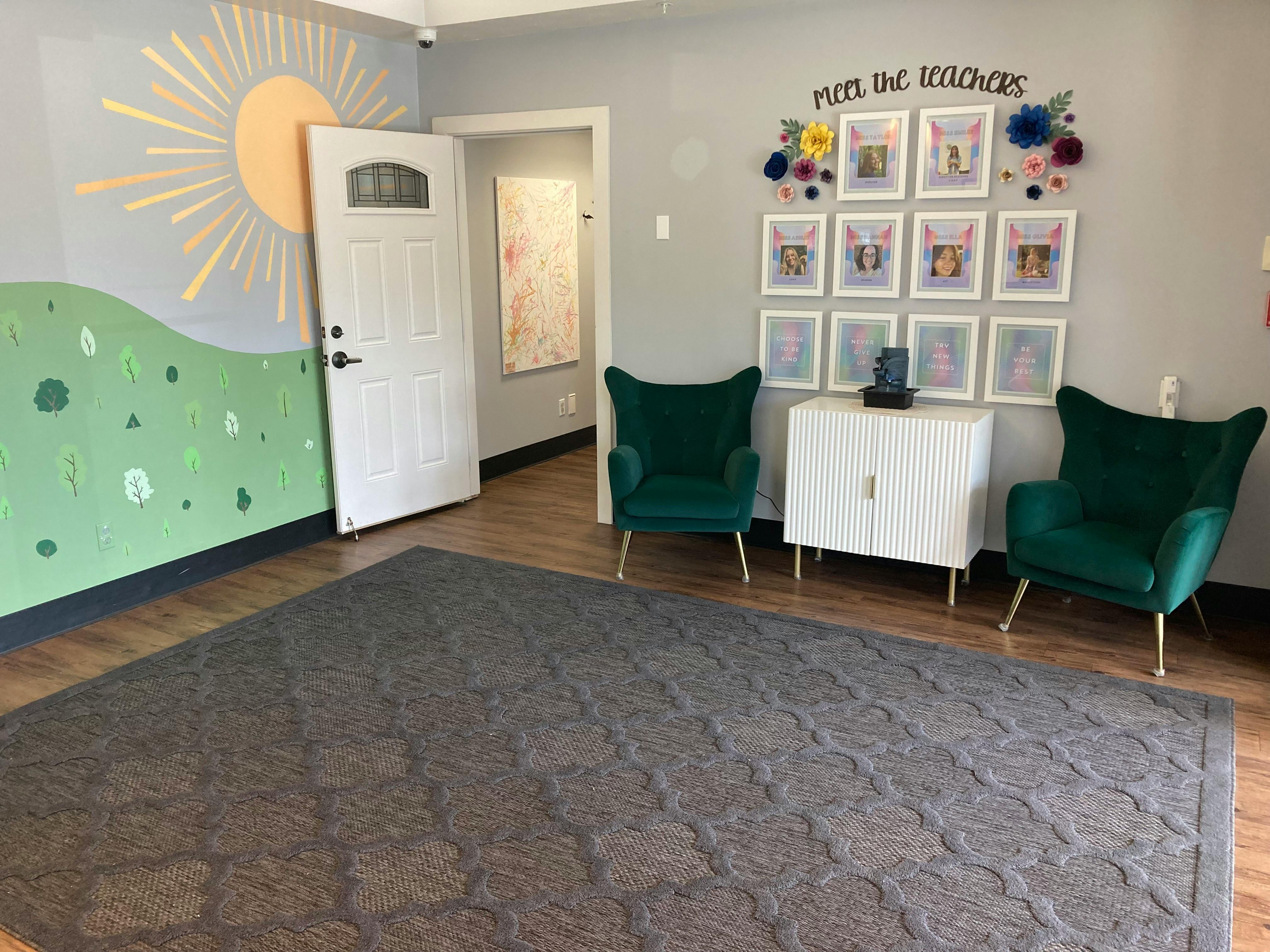 Room with a sun mural, two green chairs, and framed pictures on the wall