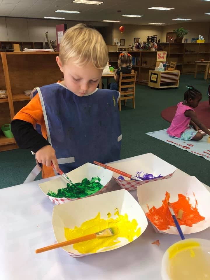 Child in a classroom painting with green paint