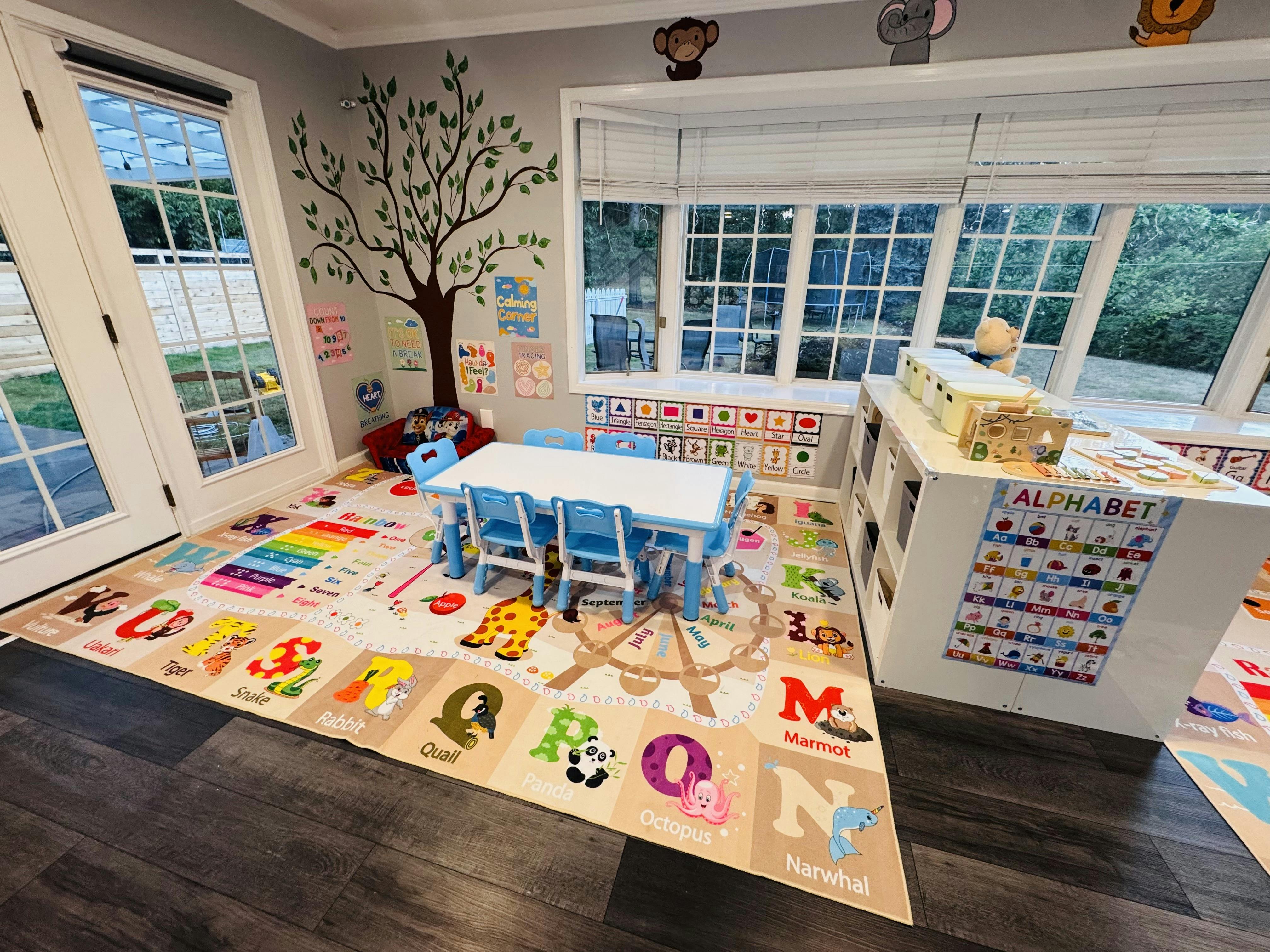 Classroom with a small table and chairs, a playmat with alphabet letters, and windows