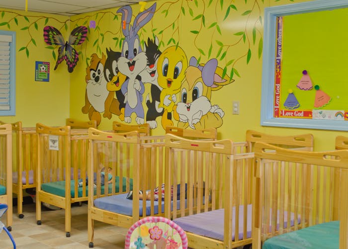 Rows of wooden cribs in a room with cartoon characters painted on the wall
