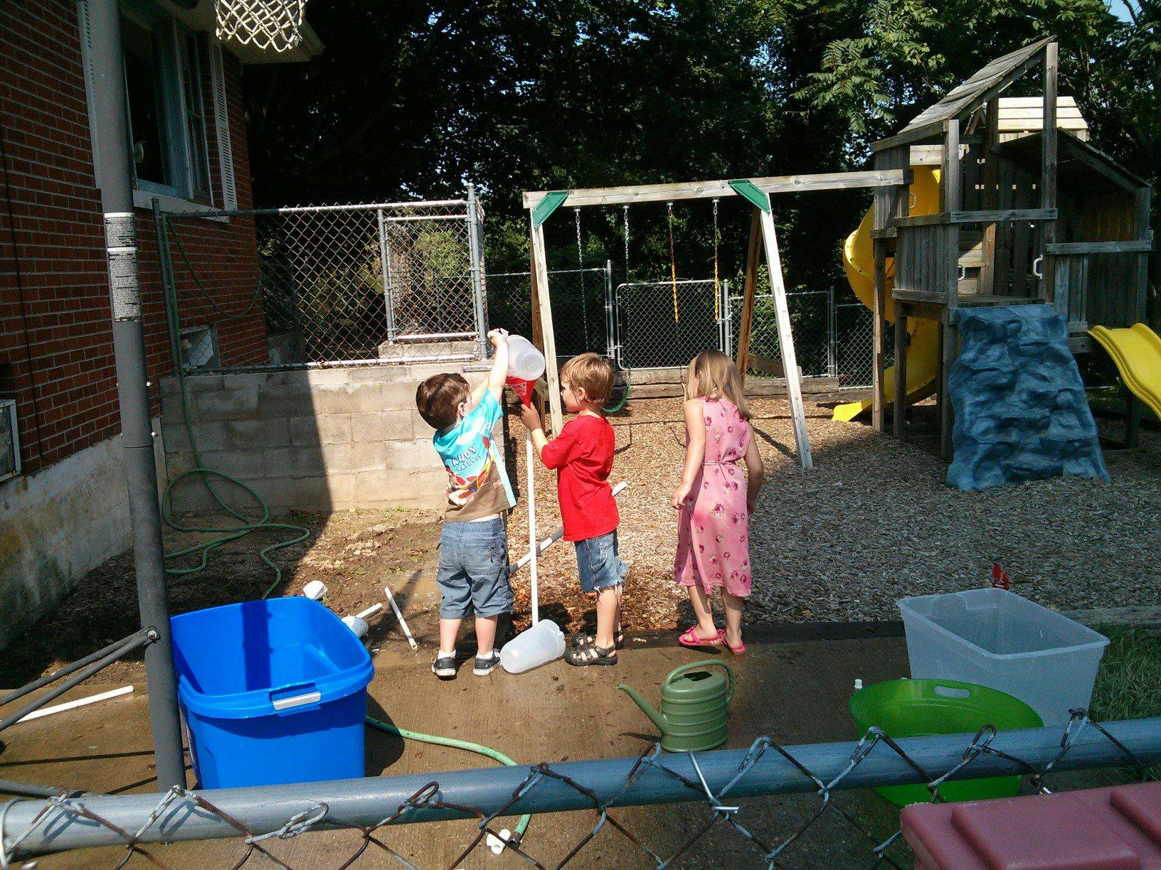 Three children playing with water and a broom on a playground