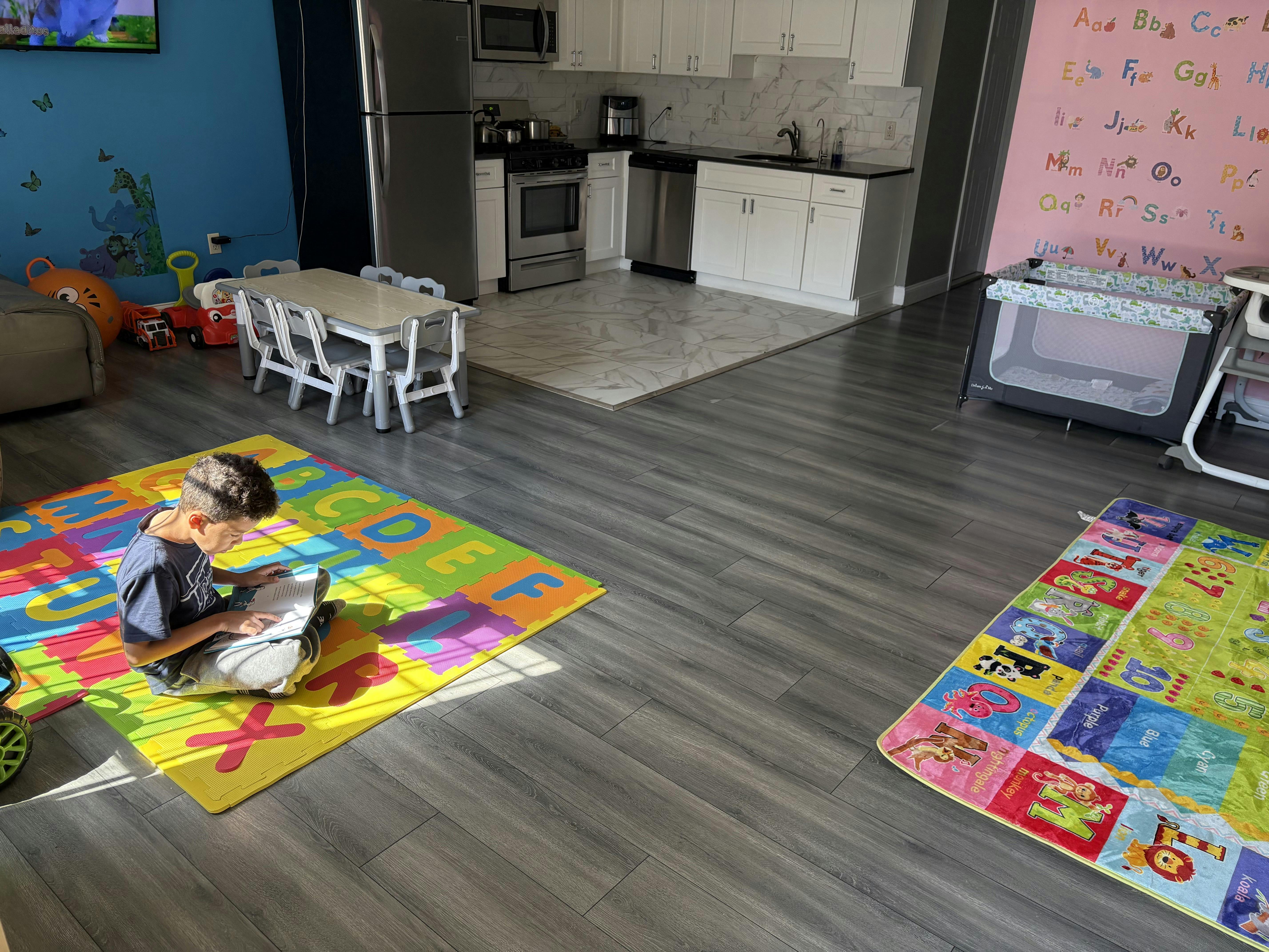 Child sitting on an alphabet floor mat reading a book in an open floor plan home