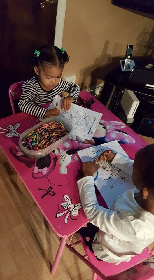Two children coloring at a pink table with crayons