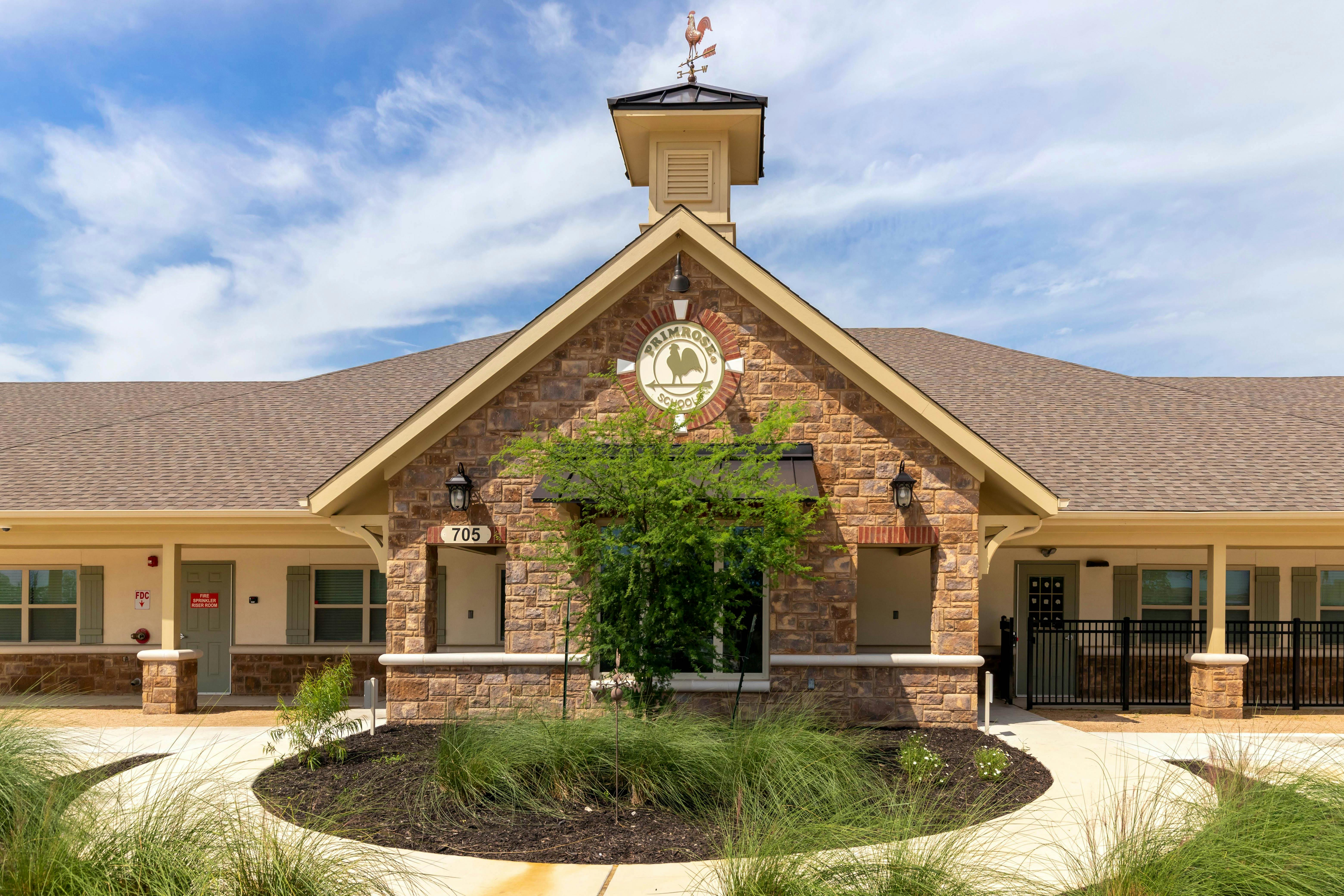 Primrose School building with a stone facade, cupola, and weather vane