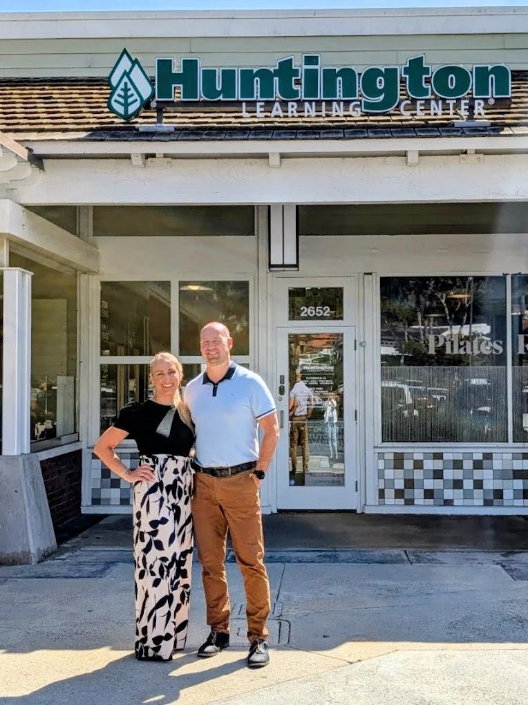 A person in a patterned skirt and a person in a polo shirt standing in front of a building