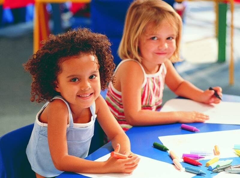 Two children at a table with paper and crayons
