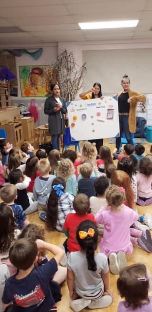 Three people presenting a poster to a group of children sitting on the floor
