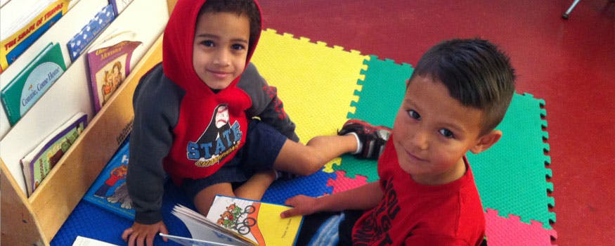 Two children sitting on floor with books in a classroom