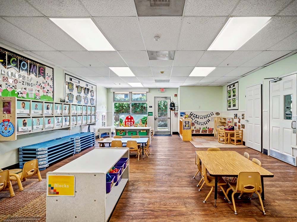Empty classroom with small tables and chairs, cubbies, and cots