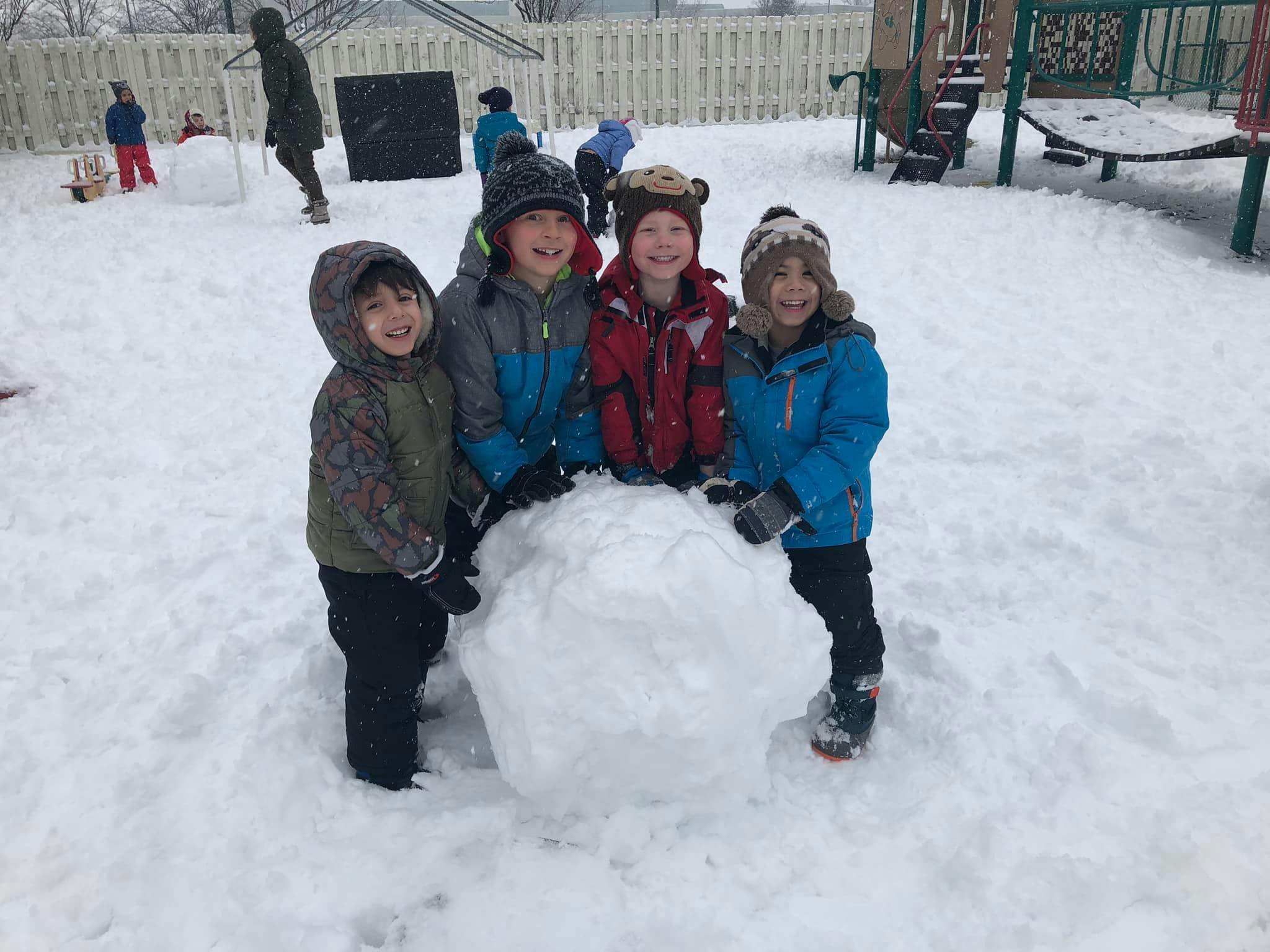Four children in winter clothes standing around a large snowball
