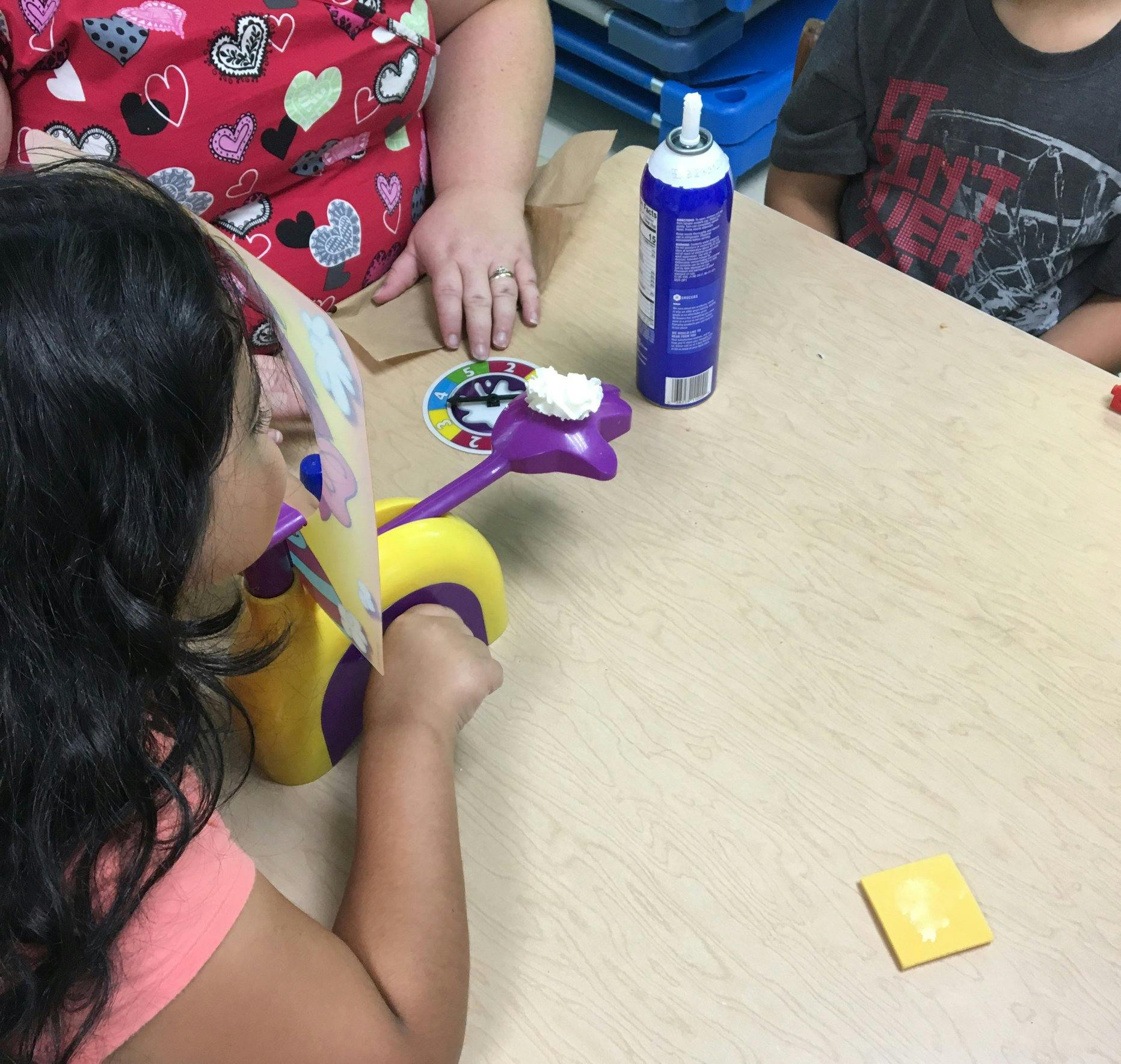 Child playing a game with whipped cream on a purple and yellow toy