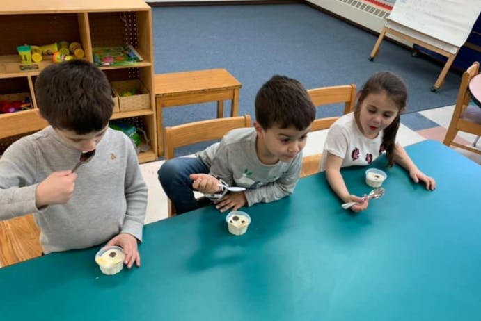 Three children eating from cups at a table in a classroom