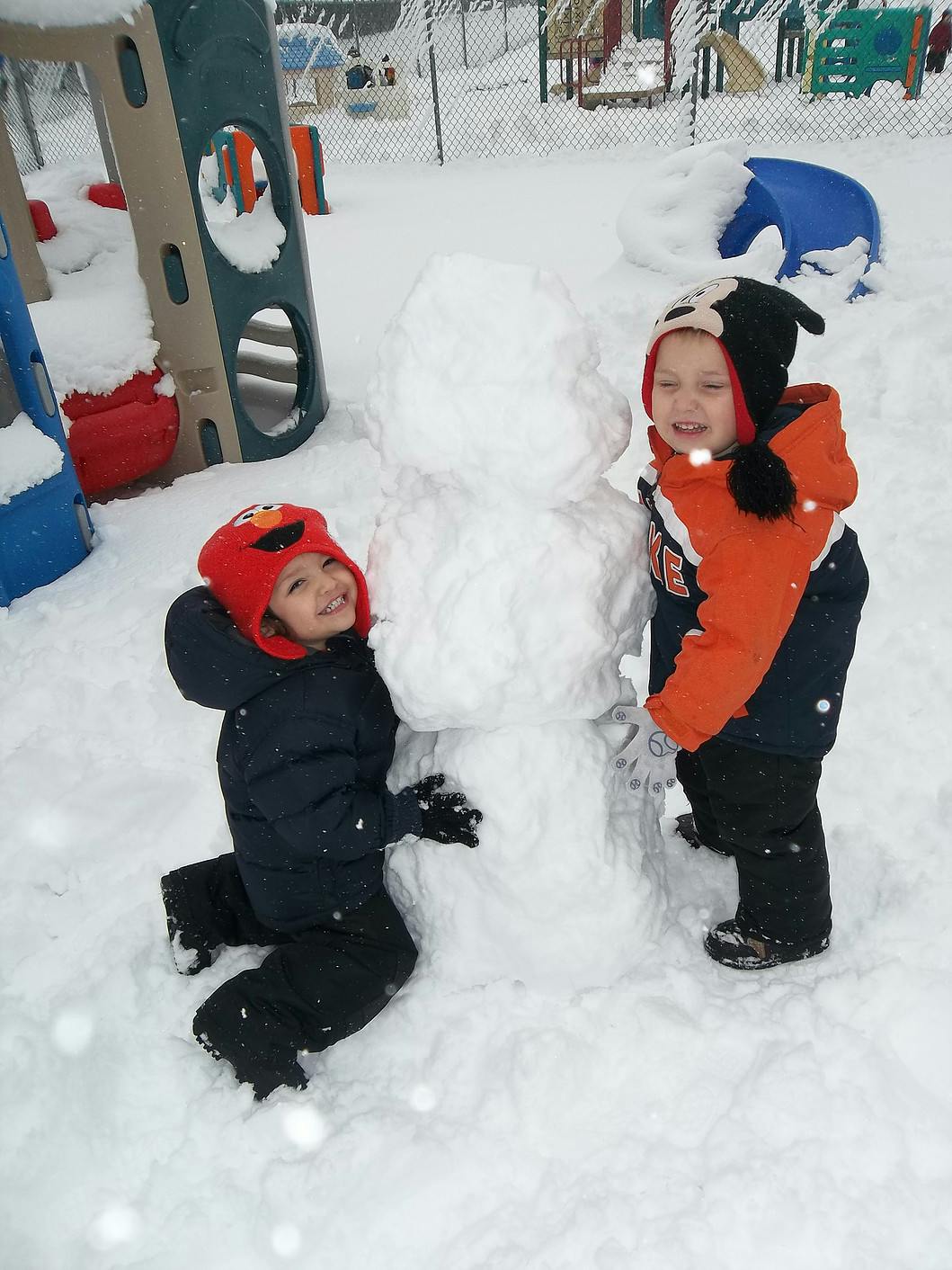 Two children building a snowman in a snowy playground