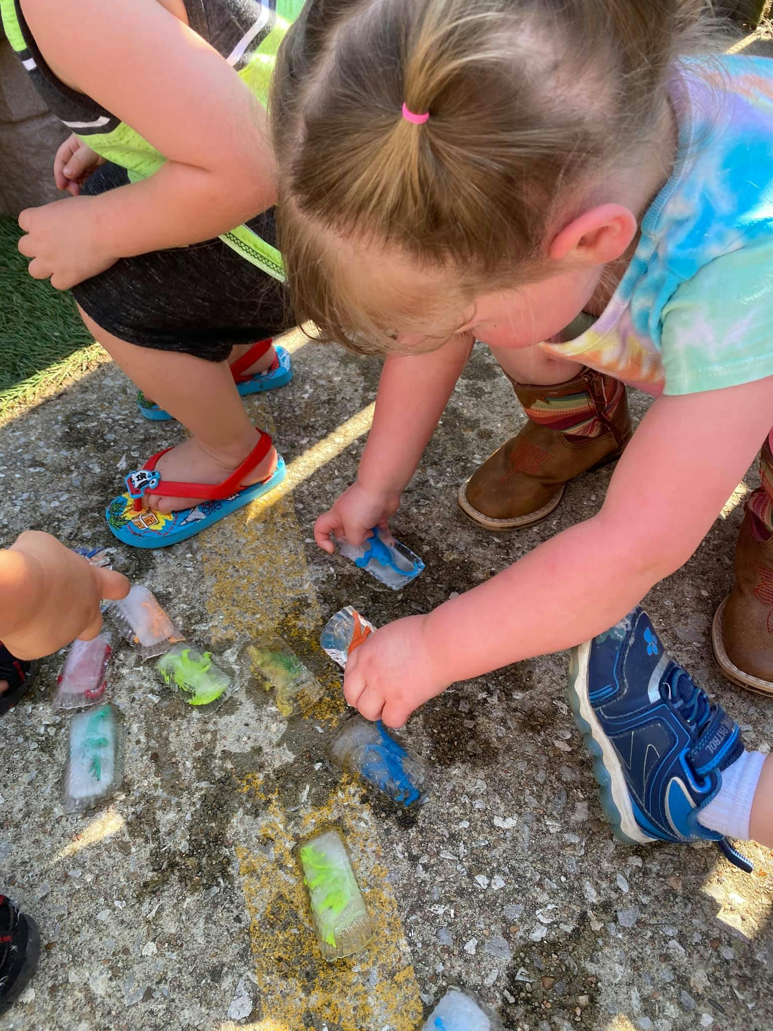 Child playing with colorful ice blocks on the ground