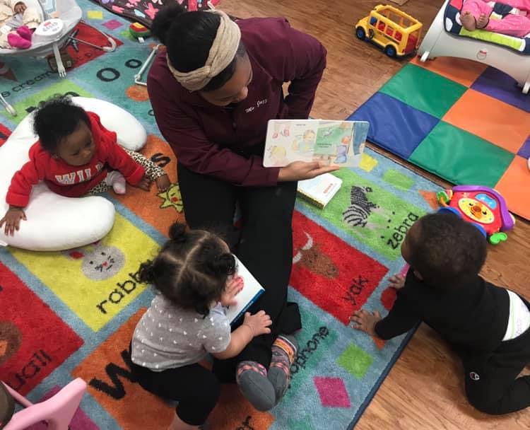 Person reading a book to three children in a classroom