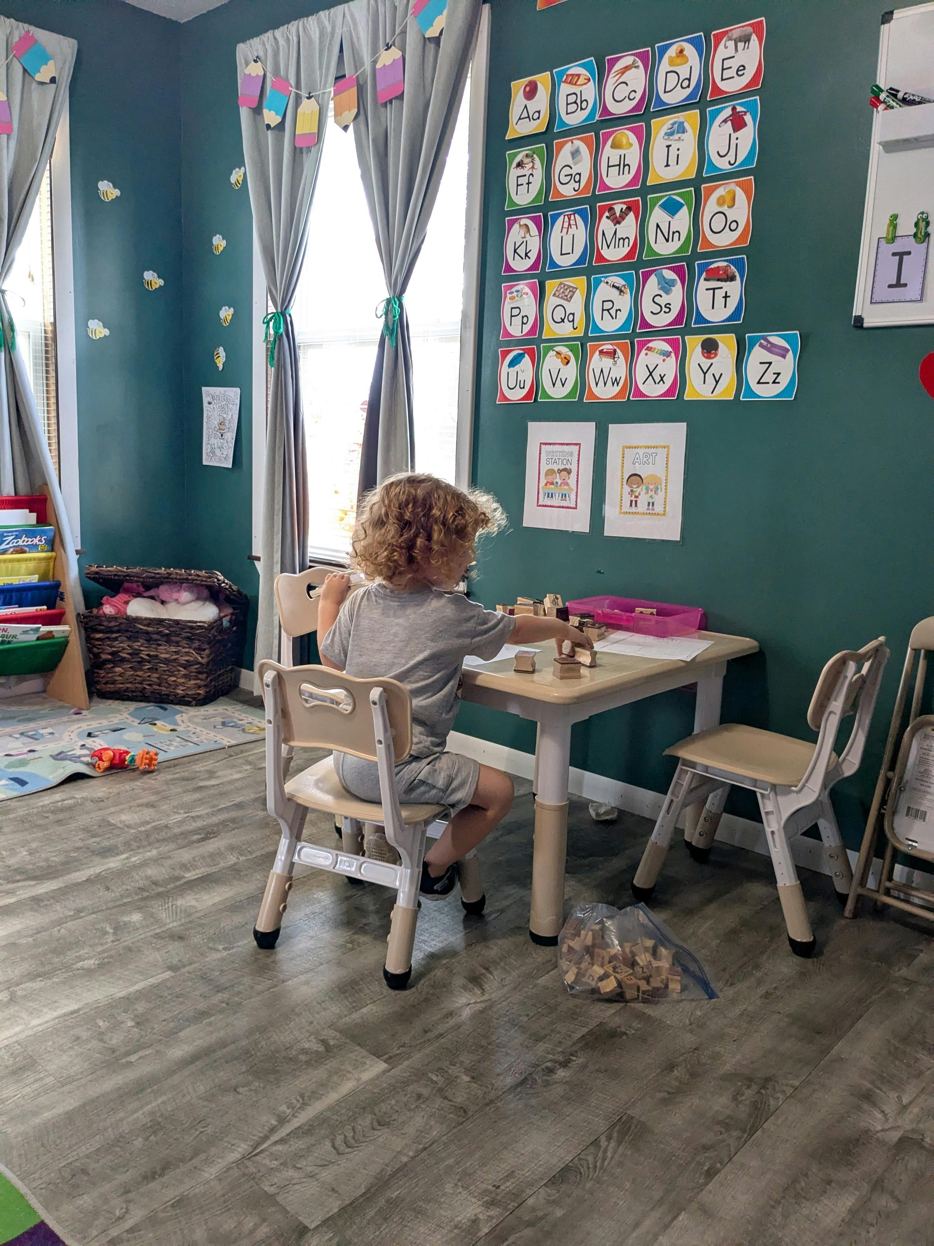 Child sitting at a small table using alphabet stamps in a playroom