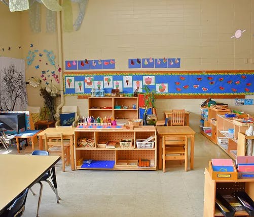 Classroom with small wooden tables, chairs, and shelves