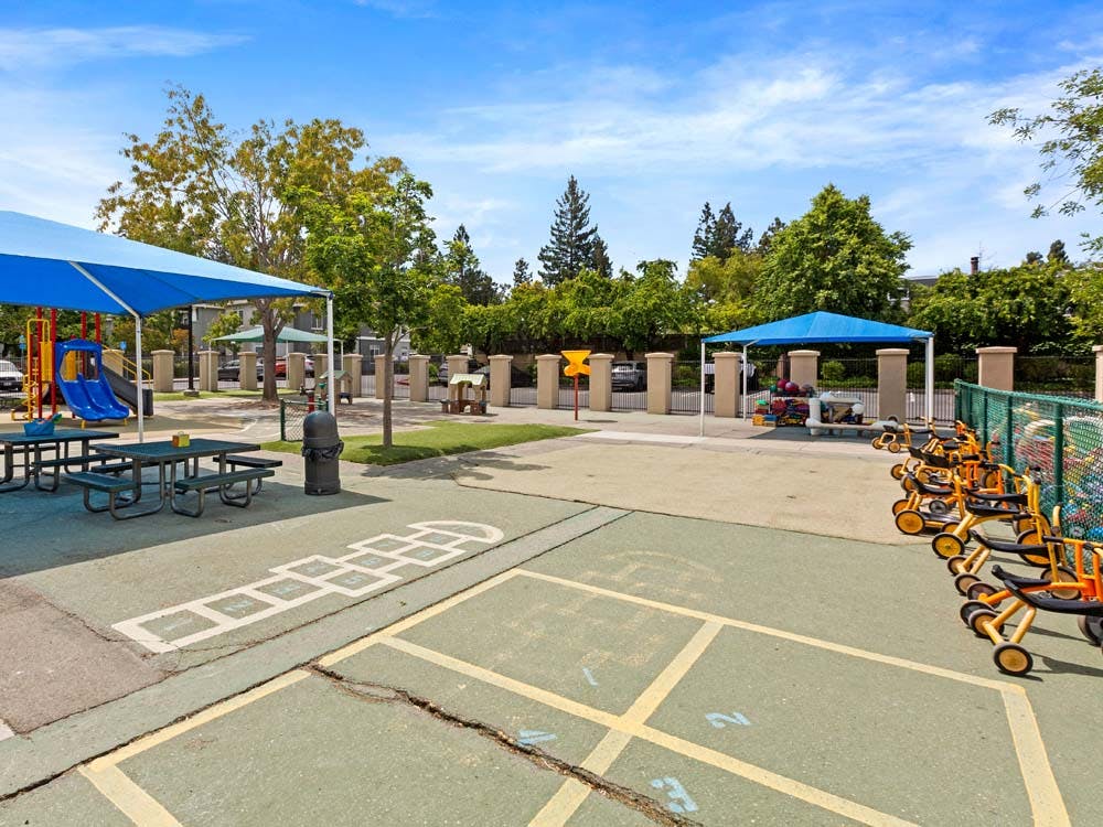 Outdoor playground with picnic tables, play structure, and tricycles