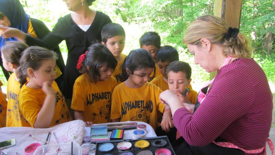 Person applying face paint to a child surrounded by other children
