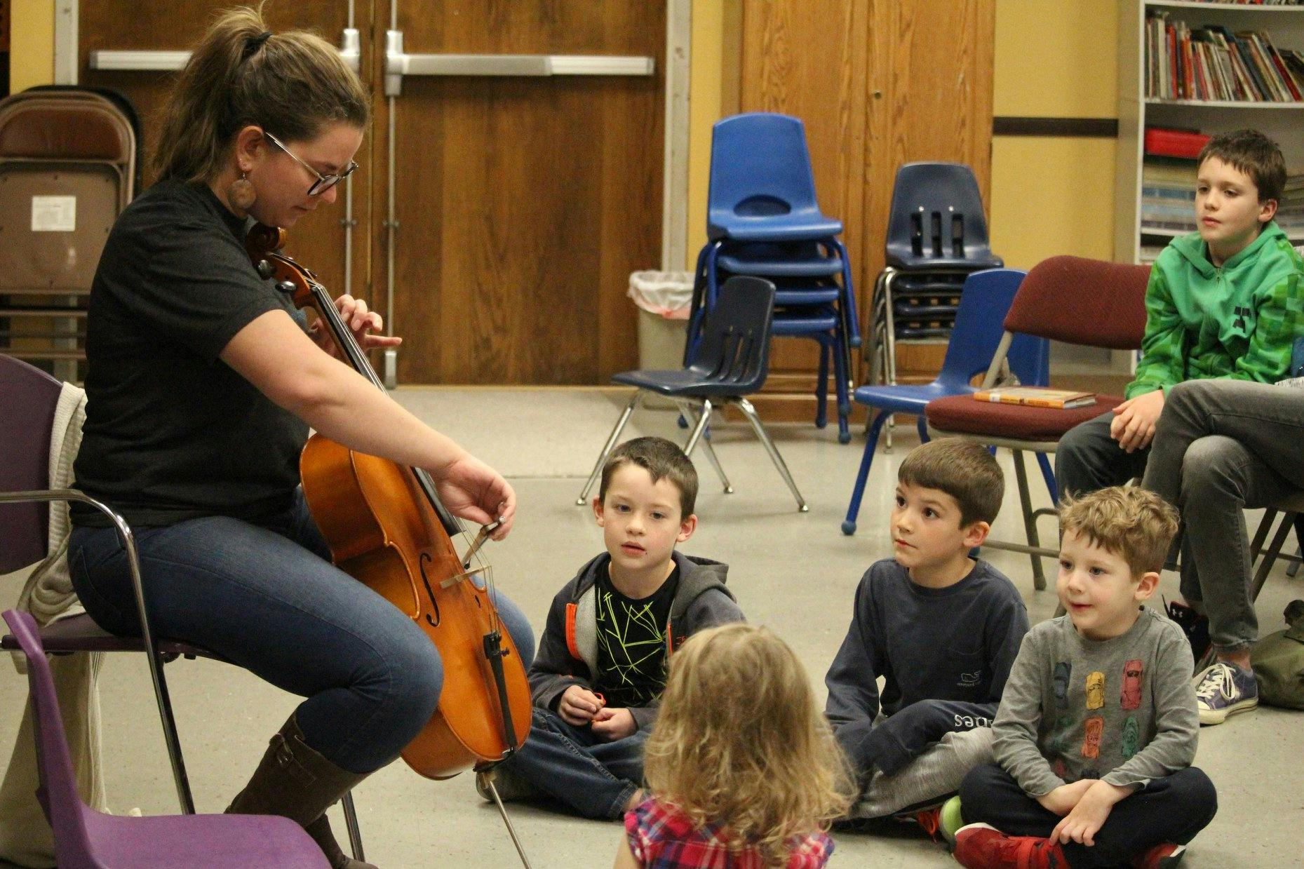 Person playing cello for a group of children