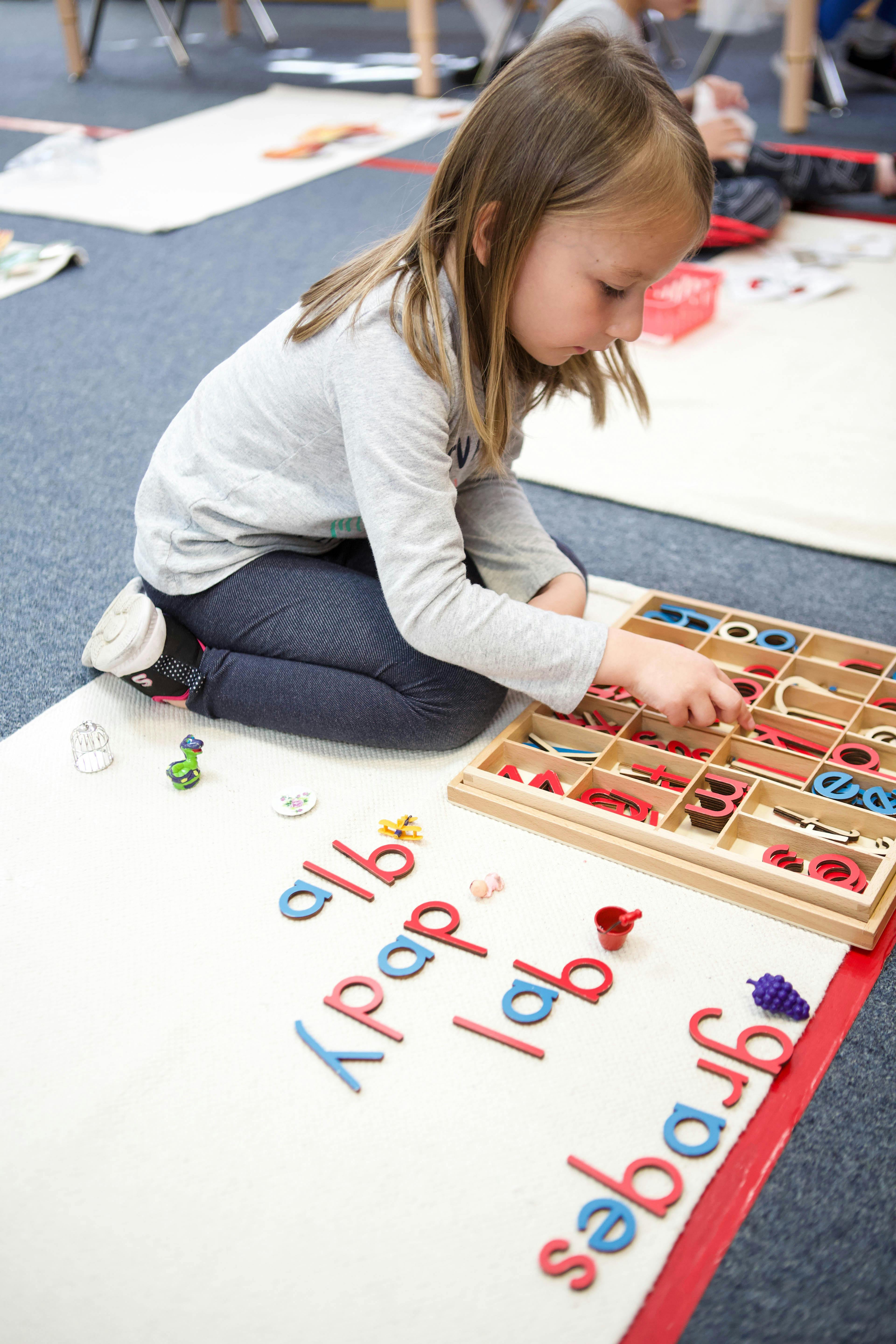 Child kneeling on floor, arranging letter cutouts on a white mat