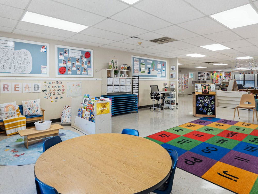 Colorful classroom with a reading corner, tables, and alphabet rug