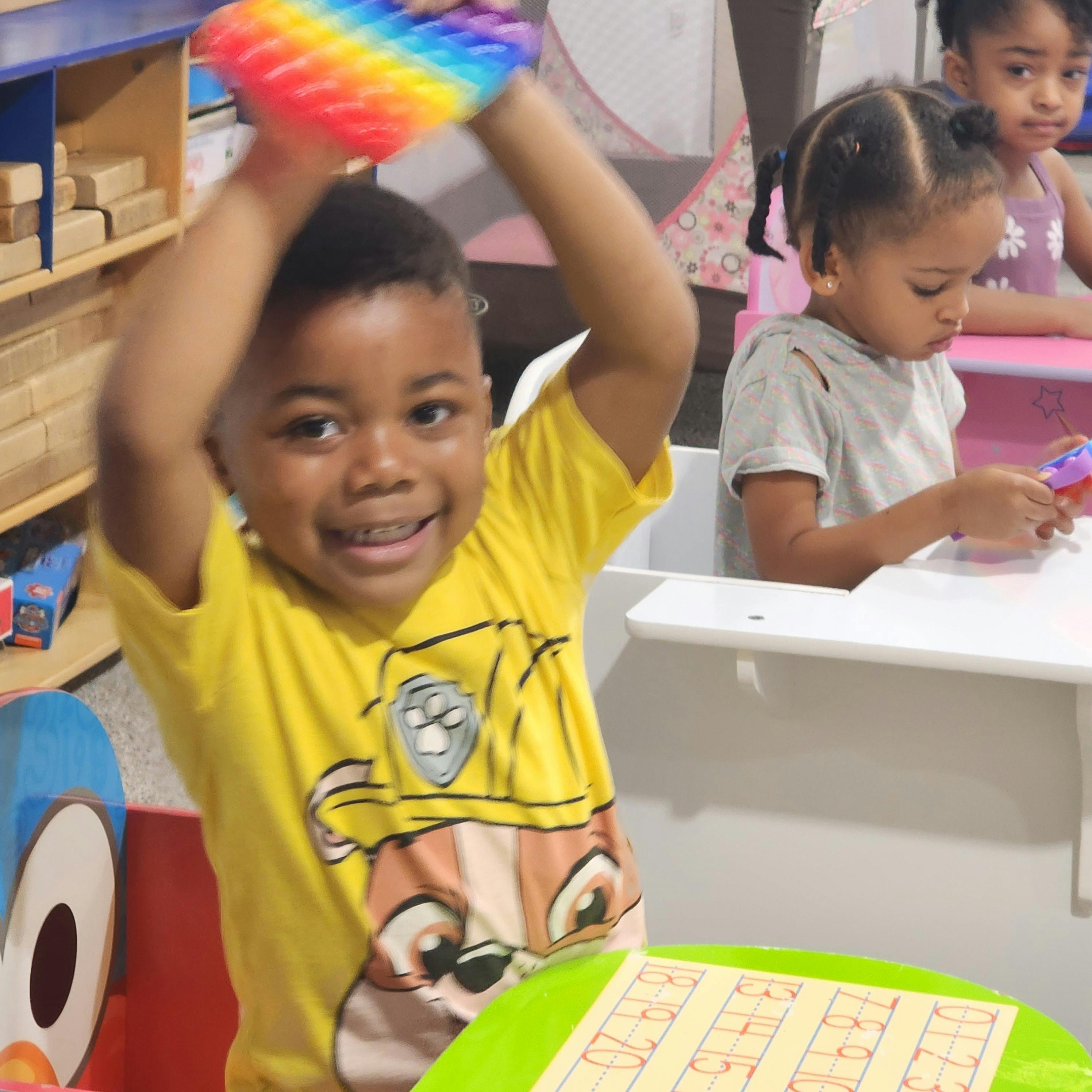 Child holding a rainbow pop-it toy above their head
