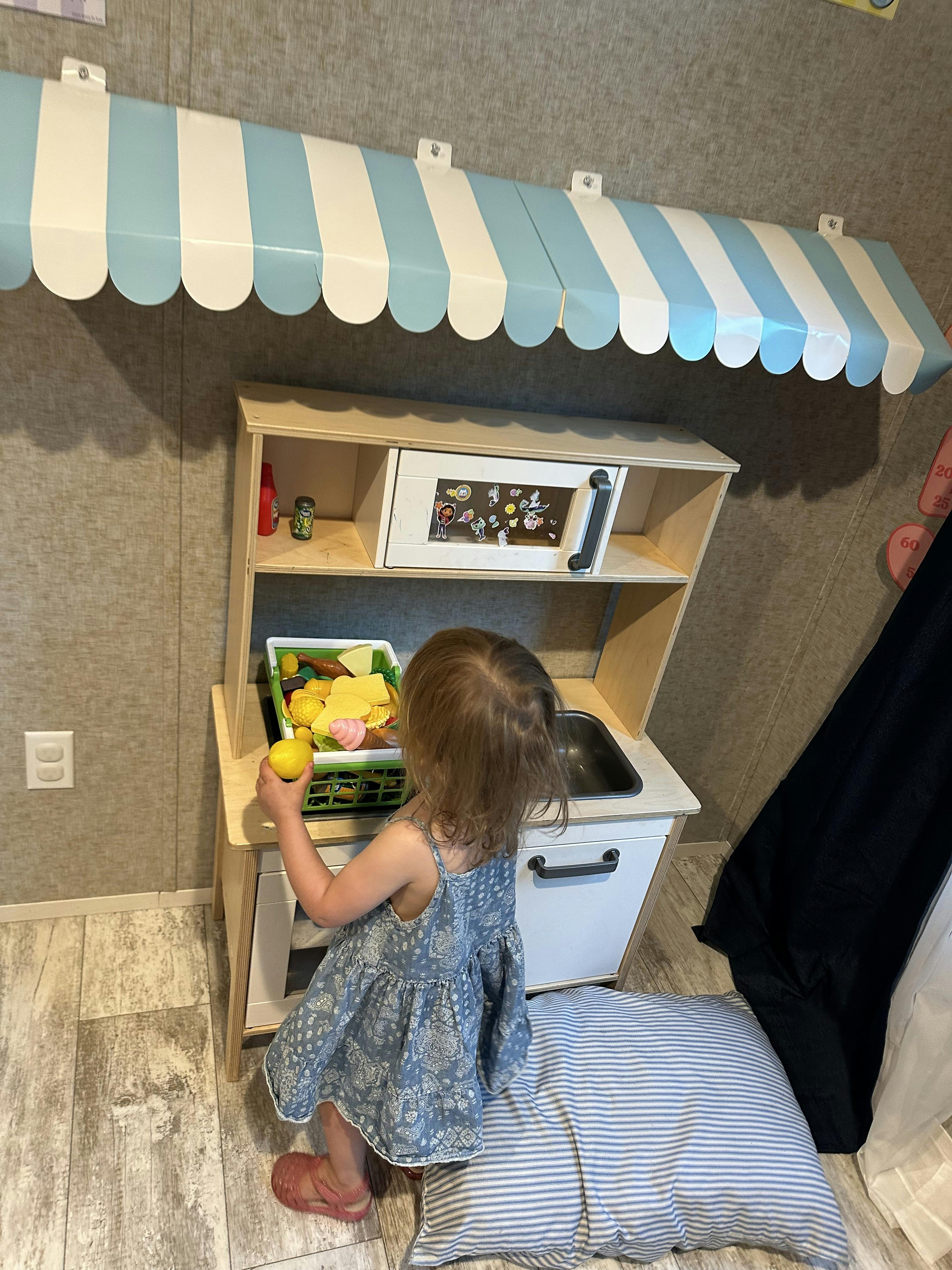 Child playing with a toy kitchen set under a blue and white striped awning