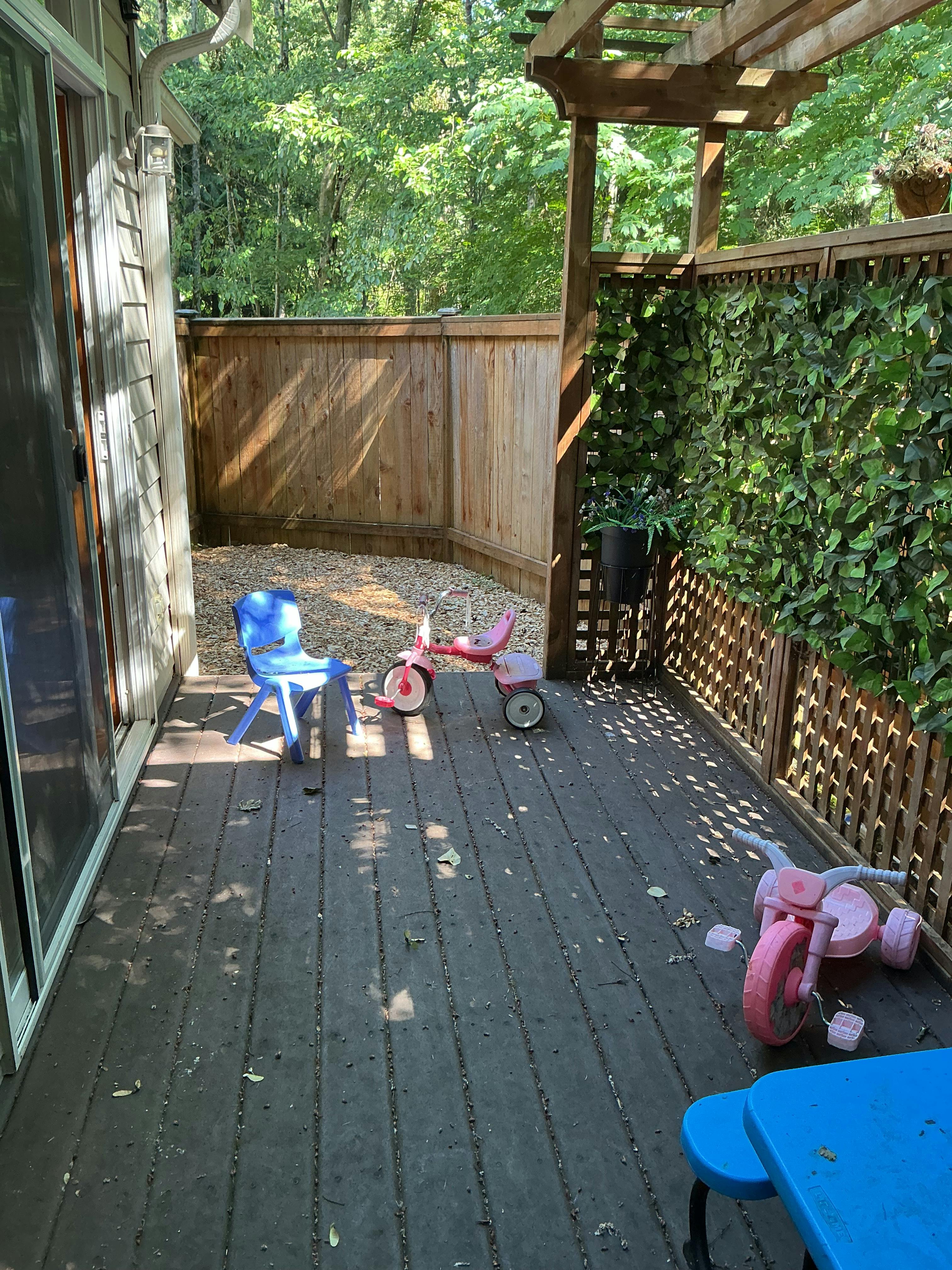 Child tricycles and a plastic chair on a wooden deck