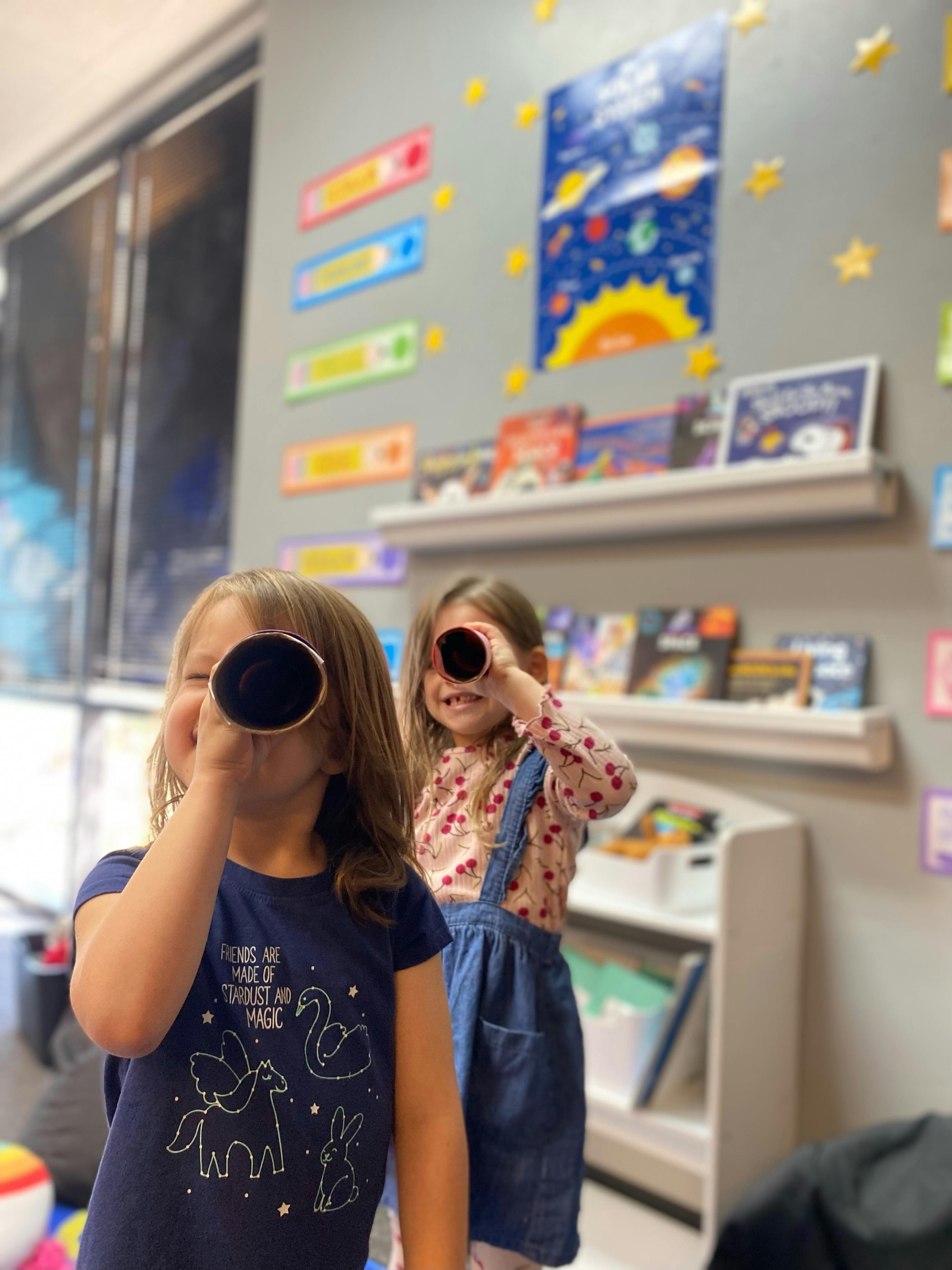 Two children looking through cardboard tubes in a classroom