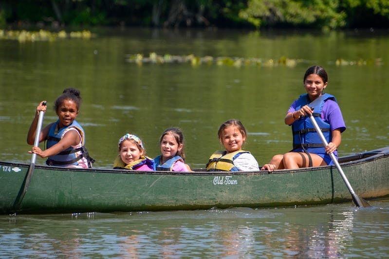 Four children in a canoe on the water, two paddling