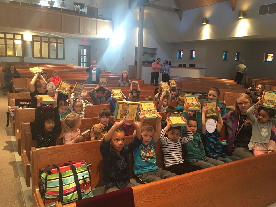 Children and adults holding books above their heads in a church