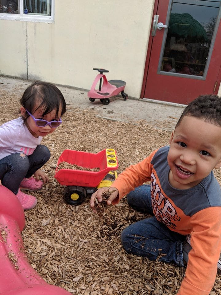 Two children playing with a toy truck on wood chips
