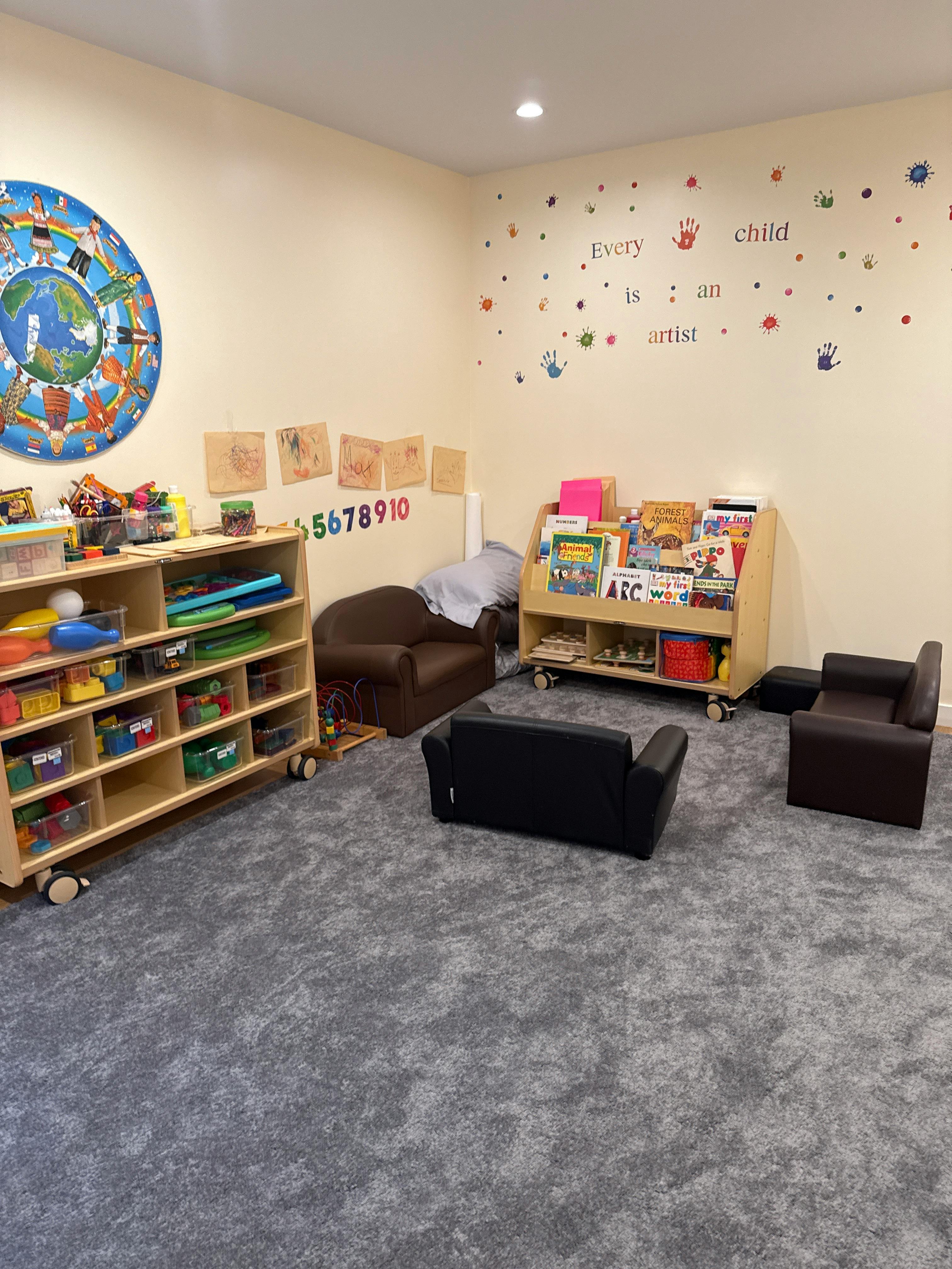 A classroom with shelves of toys and books, small chairs, and a wall decoration