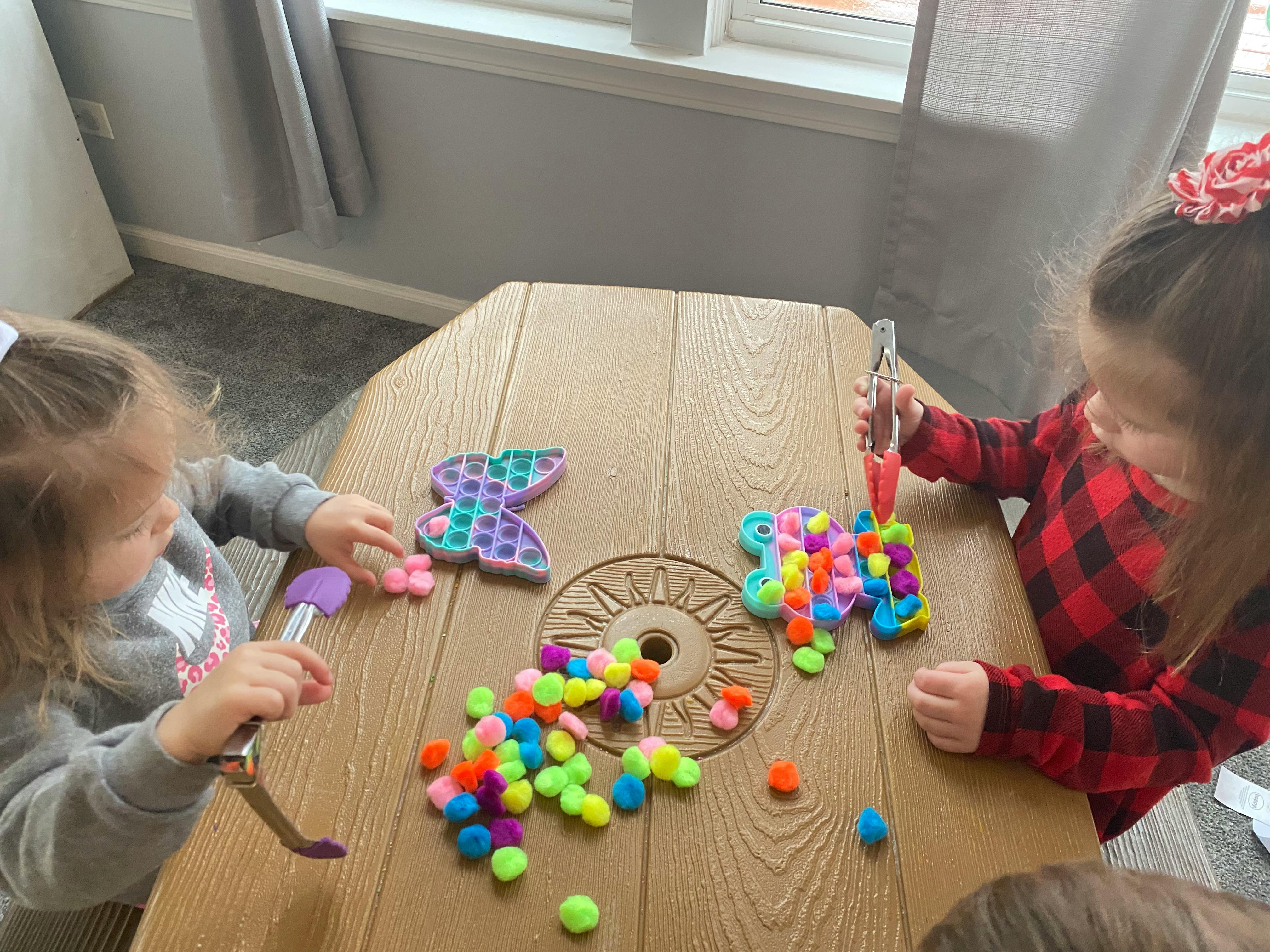 Two children playing with colorful pom-poms and pop-it toys on a table