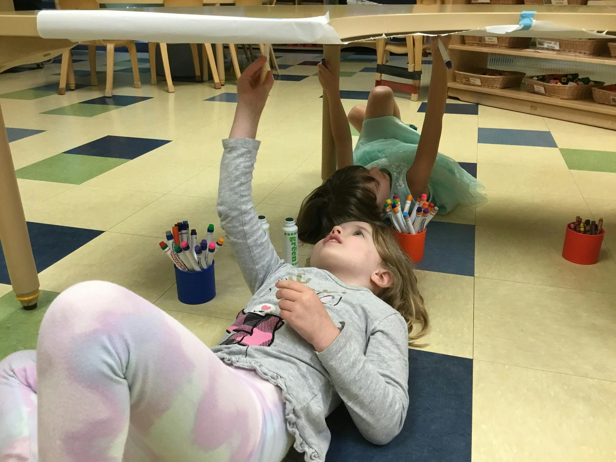 Two children lying on the floor reaching up to a table