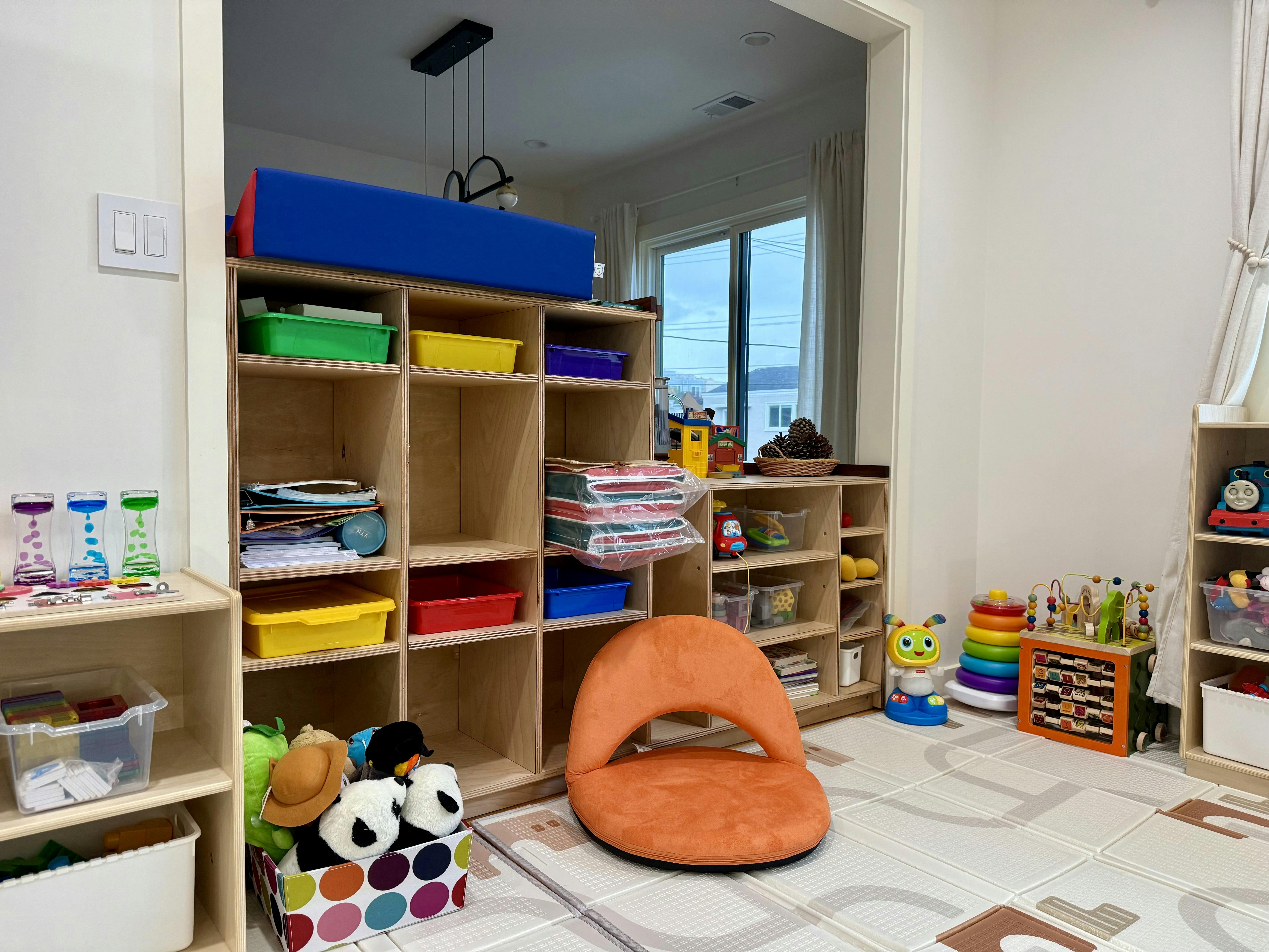 Playroom with wooden shelves, colorful bins, an orange chair, and toys