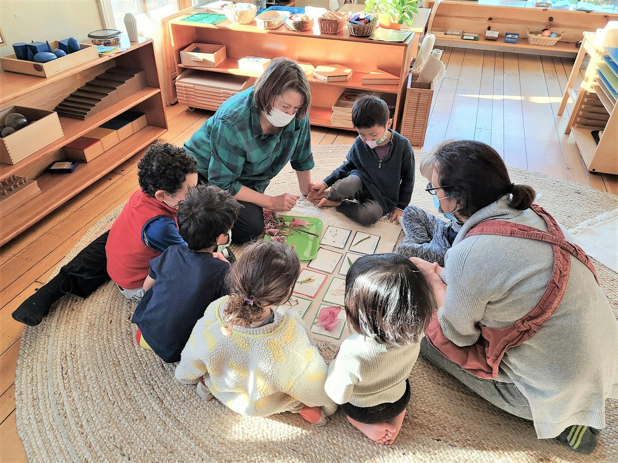Two adults and multiple children sitting on a rug, looking at items on the floor