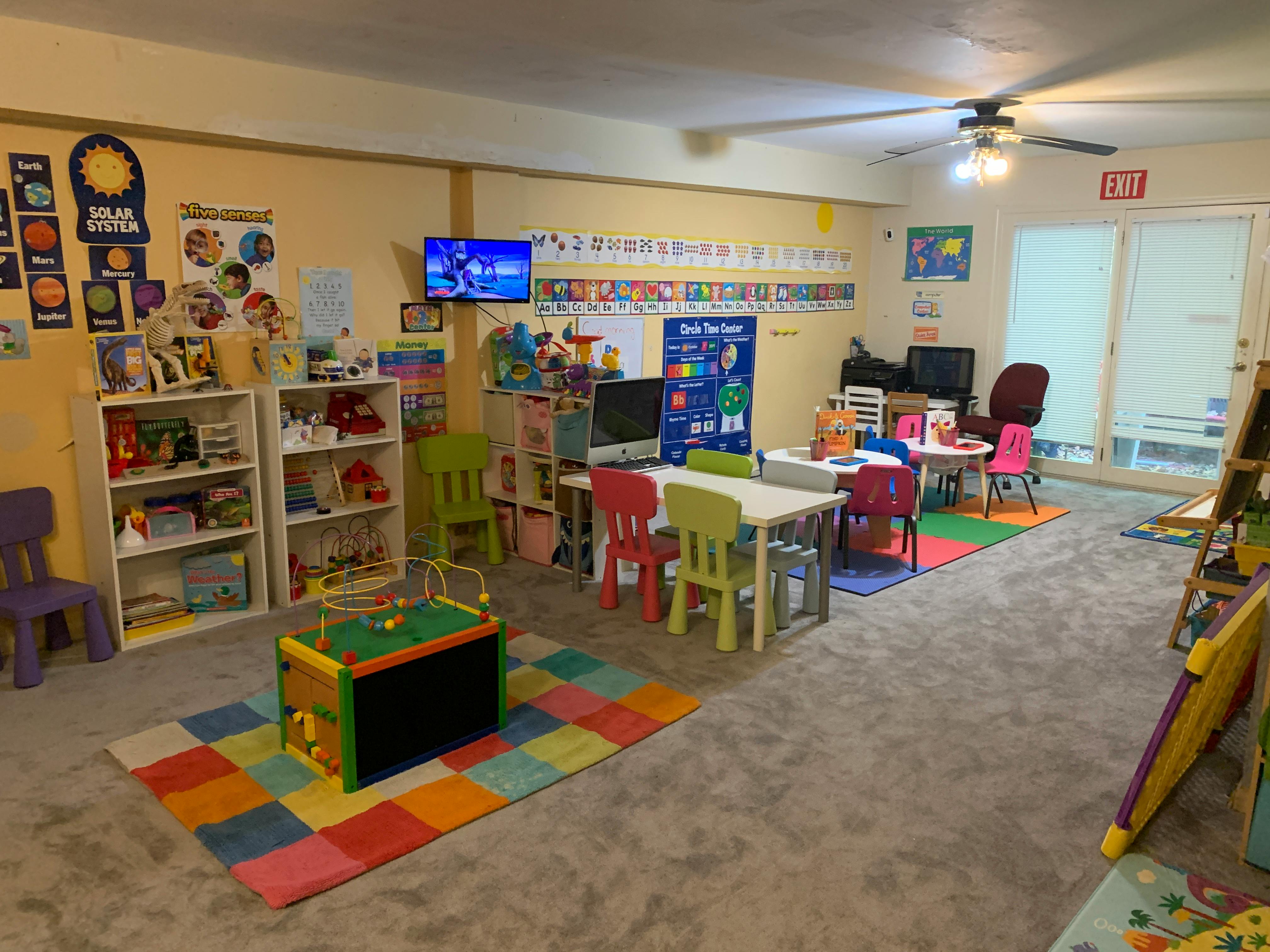 Children's classroom with small tables and chairs, bookshelves, and play area