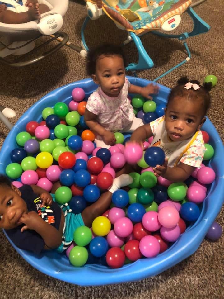 Three children playing in a blue ball pit filled with colorful balls